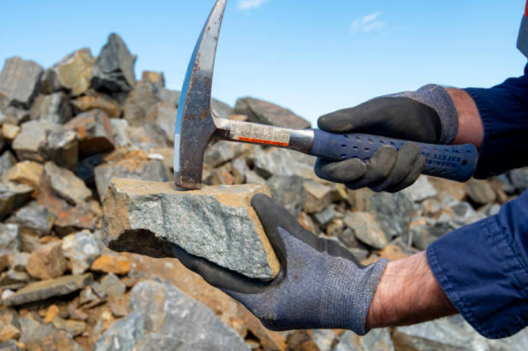 A geologist in gloves splitting a rock sample with a geological hammer at a quarry